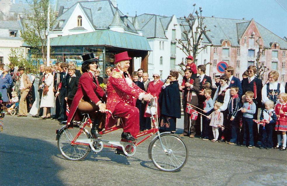 Cirkuskongen Arne Arnardo opptrådte i sin ungdom som slangemenneske, så god fysikk hadde han til langt opp i årene. Også til å sykle på tandemsykkel i 17.maitoget i Ålesund. Her har han og Anita Wagner akkurat passert Hellebroa og den gamle Brokiosken.
